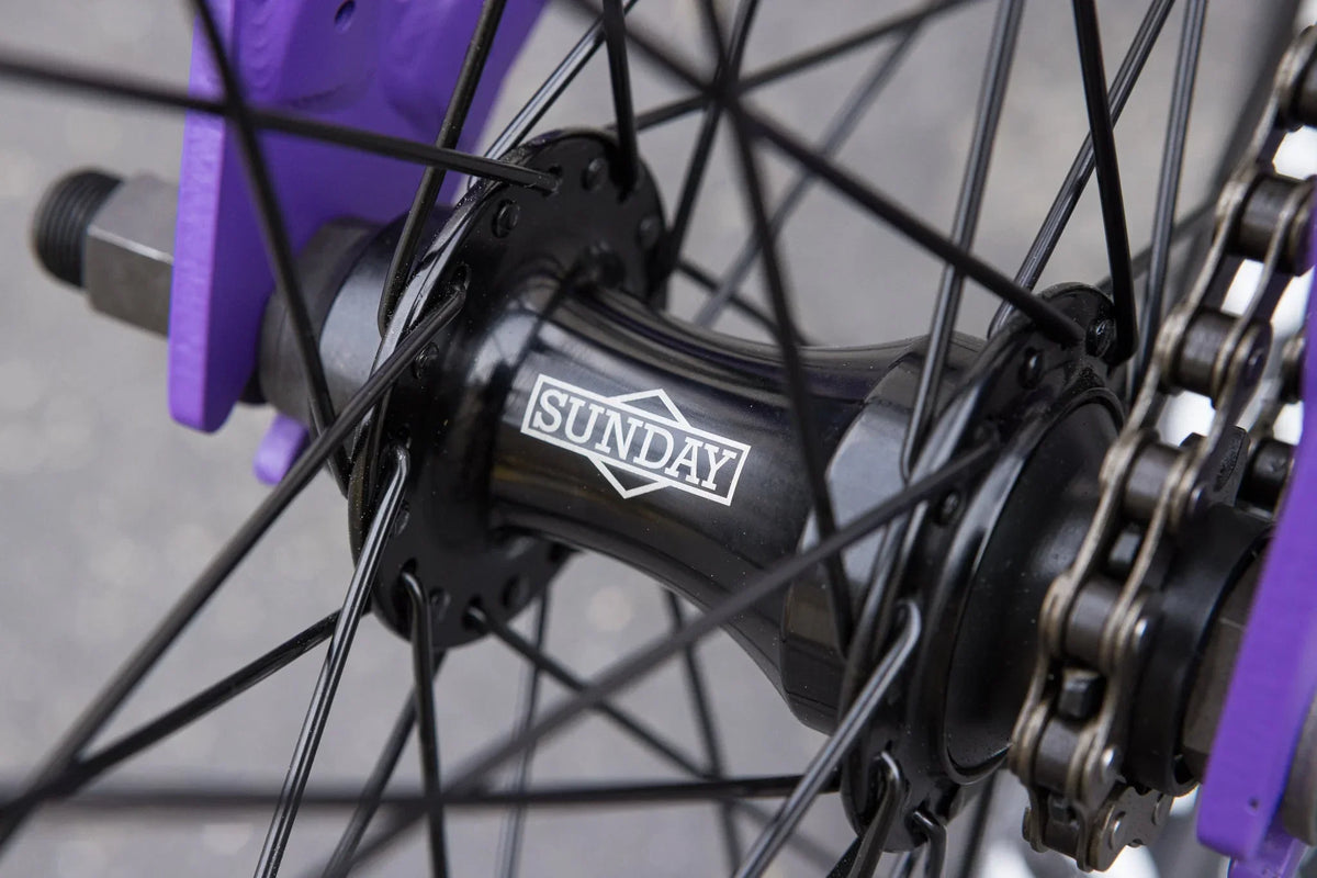 Close-up of a Sunday Forecaster BMX bike rear hub in black, mounted on a matte grape soda purple chromoly frame.