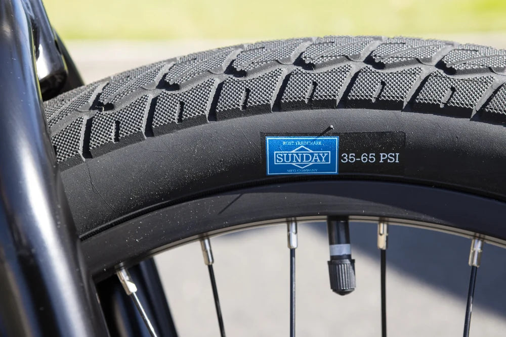 Close-up of a Sunday Current v1 tire with a blue logo decal on a black BMX rim and fork.