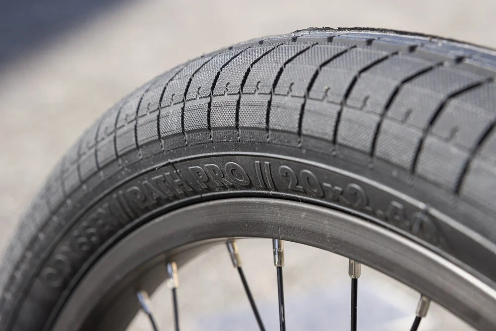 Close-up of a black Odyssey Path Pro 20x2.40 BMX tire mounted on a sealed wheel with black spokes.