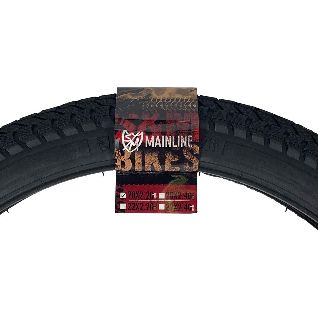 Black S&M Mainline 20-inch BMX tire with directional tread and branded paper label featuring size specifications.